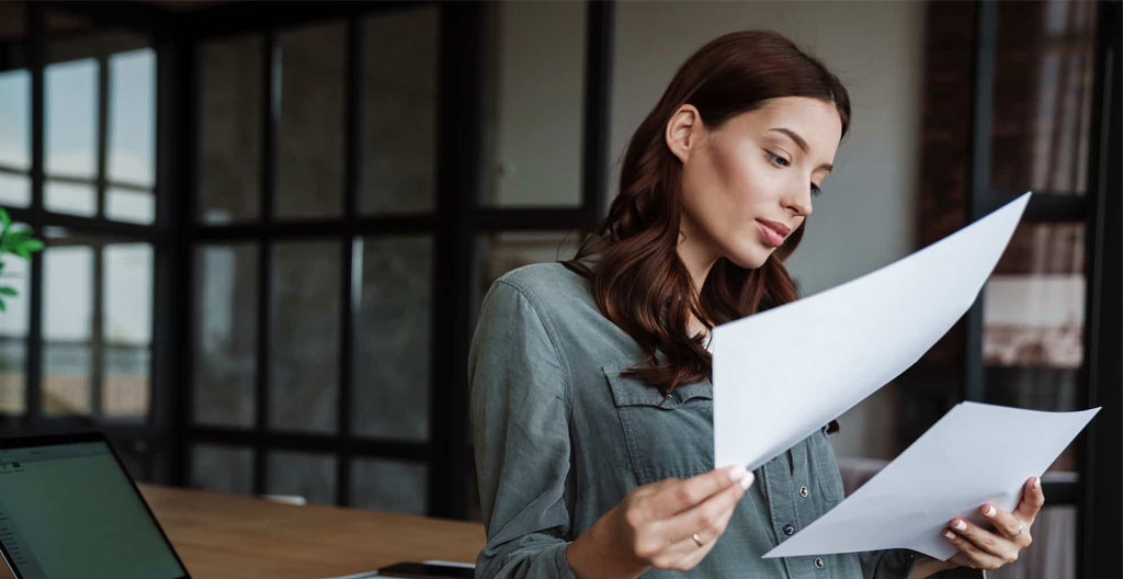 Gros plan sur des mains tenant un stylo au-dessus d'un cahier ouvert avec une tablette floue en arrière-plan sur une table en bois