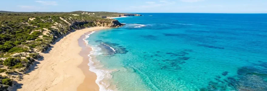 Vue aérienne d'une plage australienne aux eaux turquoise et au sable doré sous un ciel dégagé, sans présence humaine au premier plan